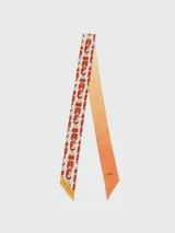 Cinta de seda Longchamp modelo Le Pliage Bandeau, con diseño reversible que combina un lado estampado con motivos de carteras y otro lado liso en degradado naranja con el logo de la marca bordado.