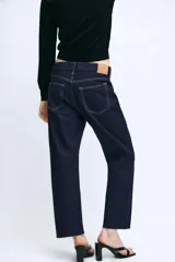 Jeans de tiro medio confeccionados en denim azul oscuro, con diseño de cinco bolsillos, trabillas para cinturón y bajo deshilachado. Cierre frontal con cremallera y botón metálico.