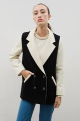 Blazer de lana con diseño bicolor, cuerpo en color negro y mangas en color crema. Presenta un corte holgado, cierre cruzado con doble botonadura y solapas amplias en contraste.