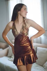 Vestido corto negro con estampado de plumas doradas, escote en V, breteles finos cruzados en la espalda, cut-outs laterales y volado en el ruedo.