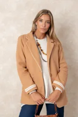 Blazer de lana soft color beige, con cierre frontal de un botón, solapas clásicas y dos bolsillos frontales con detalles de bordado artesanal en relieve. Presenta un diseño estructurado y elegante.