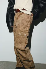 Jeans tiro medio, corte baggy balloon, color marrón claro con estampado animal moteado en tono más oscuro. Presenta bolsillos laterales, bolsillos cargo con solapa en las piernas y bolsillos de plastrón en la espalda. El bajo es ajustable con botón a presión.