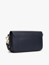 Cartera pequeña de poliuretano color azul marino con acabado liso. Presenta un diseño rectangular con solapa frontal que se cierra magnéticamente y lleva el monograma TH en metal dorado al frente. Incluye correa ajustable y extraíble para llevar al hombro o cruzada.