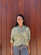 Camisa de corte holgado en color verde con estampado floral lineal en tono crema. Presenta cuello mao, cierre frontal con botones y mangas tres cuartos con puños elásticos.