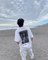 Remera de manga corta blanca con diseño gráfico en la espalda estilo estampilla que muestra una fotografía en blanco y negro de una persona con un gato, acompañada del logotipo rojo de Kaboa Industries.