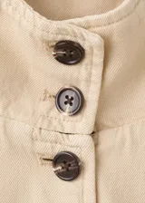Chaqueta de algodón estilo denim, de diseño oversize, color beige, con cuello alto, manga larga, bolsillos de parche con solapa y cierre frontal de botones oscuros.