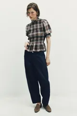 Blusa de cuello subido con diseño de cuadros en tonos marrones, negros y blancos. Presenta mangas cortas con terminación en volantes y un corte ajustado con detalle de volado en la cintura.