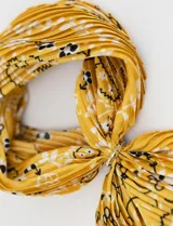 Bandana de satén plisado color amarillo con estampado de flores blancas y negras. Incluye un anillo metálico plateado para ajustar.