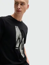 Camiseta negra de manga corta y cuello redondo, con un gráfico abstracto en blanco y negro con textura desgastada en el centro del pecho, y el logo 'BOSS' en la parte inferior izquierda del gráfico.