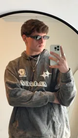 Buzo gris nevado con capucha y bolsillo tipo canguro. Estampado frontal con la palabra "BASED" y un logo.