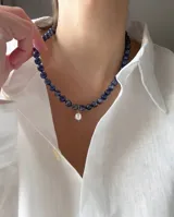 Collar de cuentas de piedra sodalita azul con un dije colgante de perla natural en el centro y cierre tipo marinero dorado.