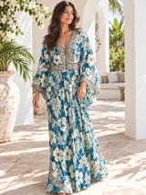 Vestido largo de estilo bohemio, color azul con estampado floral en tonos blancos y detalles geométricos en el escote y la cintura. Posee escote en V con cordones ajustables, mangas amplias tipo kimono y una silueta fluida y holgada.