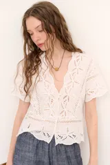 Camisa azul de manga corta confeccionada en tejido broderie con diseño calado y floral. Cuenta con escote en V y cierre frontal de botones.