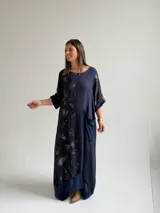 Vestido largo azul oscuro con diseño asimétrico que combina un lado liso con un lado estampado de hojas, manga corta y bolsillo frontal aplicado.