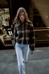 Chaqueta de corte recto con cuello solapa y cierre frontal de botones. Presenta un diseño de cuadros en tonos oscuros y beige con textura de lana.