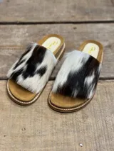 Sandalias bajas con base color suela y capellada de piel de vaca con manchas marrones y blancas.