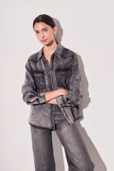 Camisa de denim celeste con cuello clásico, cierre frontal con botones a presión, dos bolsillos con solapa abotonada en el pecho y mangas largas con puños abotonados.