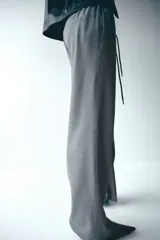 Pantalón de corte holgado color gris, con cintura elástica y cordón de ajuste trenzado en tonos rojo y blanco. Presenta piernas rectas y bolsillos laterales.