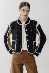 Chaqueta de punto con diseño color block en negro, beige y marrón. Presenta cuello redondo, cierre frontal con botones grandes, bolsillos frontales y detalles de costuras decorativas verticales en color claro.