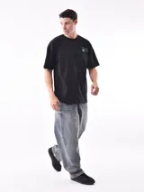 Remera negra de corte oversize con cuello redondo y manga corta. Presenta un pequeño estampado en el pecho con texto en color verde azulado.