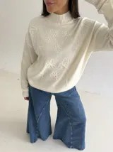 Sweater de punto color blanco con cuello polera, manga larga y diseño bordado al tono con motivos florales en el frente y las mangas.