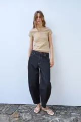 Top de punto color beige con cuello subido, manga corta y diseño texturizado con efecto arrugado. Presenta aplicaciones de perlas distribuidas en la parte frontal y las mangas.