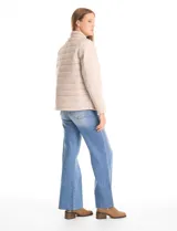 Campera 3 en 1 de color beige, con sistema de capas desmontables. La capa exterior es de tejido técnico resistente al viento y lluvia ligera, con capucha fija, cierre frontal con solapa, bolsillos de parche y ajuste elástico interno en la cintura. Incluye una campera interior capitoneada ultraliviana que puede usarse de forma independiente.