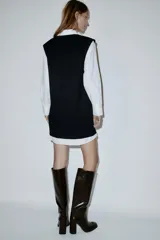 Vestido corto que combina una camisa blanca de manga larga con cuello solapa y botones frontales, con un chaleco de tejido negro de punto con escote en V.