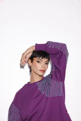 Buzo violeta de jogging con friza, corte holgado y mangas balloon. Tiene un estampado bordado con lurex.