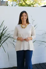 Sweater de tejido de punto en color beige, con cuello redondo, mangas tres cuartos y corte holgado con ruedo ligeramente más largo en la parte posterior.