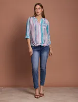 Blusa de gasa con estampado de rayas verticales en tonos celestes, violetas y blancos. Presenta cuello mao con escote en V, cierre frontal con botones, bolsillo aplicado en el pecho y mangas largas con presilla para regular el largo. El diseño incluye un nudo en la parte inferior delantera.