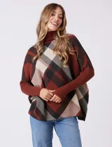 Polera estilo poncho de corte oversize, con cuello alto tejido y mangas largas con puños elásticos. Presenta un diseño de estampado a cuadros en tonos bordó, beige y negro.
