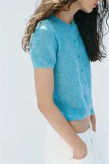 Chaqueta de punto confeccionada con mezcla de lana y alpaca, color celeste, de manga corta, cuello redondo y cierre frontal con botones.