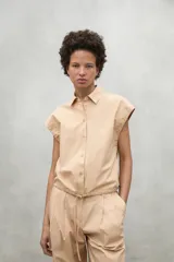 Camisa color beige con cierre frontal de botones y dobladillo ajustable con cordones de tela.