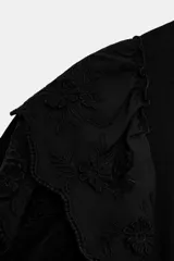 Camiseta de cuello redondo y manga corta, color negro, con detalle de volantes laterales bordados a tono.