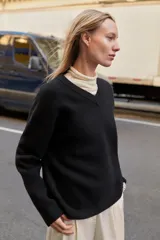 Jersey de punto negro, con cuello en V (pico) y manga larga, acabado en rib en puños, cuello y bajo.