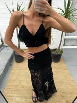 Pollera larga asimétrica color negro, confeccionada en encaje con detalles de terciopelo, de tiro alto y diseño con movimiento y vuelo en el bajo.