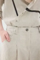 Pantalón de lino marrón de tiro medio, con calce holgado y diseño de piernas amplias. Cuenta con bolsillos traseros, trabillas para cinto y un pin bordado en contraste.