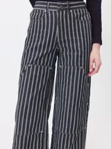 Pantalón de tiro medio y pierna ancha confeccionado en denim de algodón grueso. Presenta un diseño a rayas verticales en tonos azul y celeste, con costuras en contraste color rojo, bolsillos laterales tipo cargo y remaches metálicos.