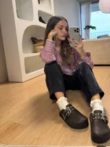 Zuecos de cuero color marrón oscuro con hebilla y detalles de ojalillos metálicos.