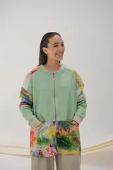 Campera larga con cierre metálico y bolsillos grandes, de color verde con mangas y parte inferior estampadas con diseño abstracto multicolor.