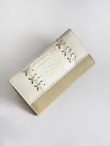 Billetera de cuero con diseño bicolor en tonos crema y beige. La solapa presenta una textura tipo reptil y detalles decorativos de cordones cruzados en los laterales. Cuenta con cierre mediante broche y monedero externo.