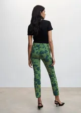 Pantalón de vestir de corte skinny con estampado floral en tonos verde claro y verde oscuro. Presenta tiro medio, trabillas para cinturón, cierre con cremallera y botón, y bolsillos laterales y traseros. Confeccionado en tejido fluido con forro interior.
