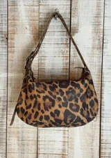 Bolso de hombro tipo hobo con acabado texturizado efecto craquelado en tonos beige y blanco. Cuenta con una correa ajustable con hebilla metálica, cierre superior y diseño espacioso.