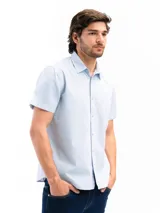 Camisa de manga corta color celeste claro, confeccionada en algodón, con cuello clásico y un bolsillo de parche en el lado izquierdo del pecho.