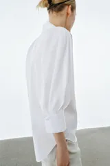 Camisa de algodón con cuello redondo y escote en pico, de manga tres cuartos con puños y bajo asimétrico redondeado.