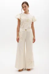 Pantalón de lino color crudo, de corte amplio y tiro alto con cierre frontal. Presenta un bordado artesanal en hilo beige con diseño floral abstracto en el lateral del bolsillo.