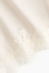 Bombacha tipo shortie de tiro alto, color crema o blanco roto, confeccionada en microfibra lisa con un amplio ribete de encaje floral en el ruedo inferior.