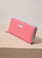 Billetera de cuero sintético con cierre perimetral, color fucsia en el exterior y celeste en los fuelles, con placa metálica grabada con el logo de la marca.