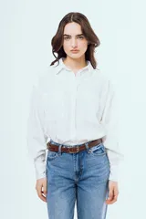 Camisa blanca de manga larga, corte oversize, con cuello camisero, cierre frontal con botones y dos bolsillos aplicados en el pecho.